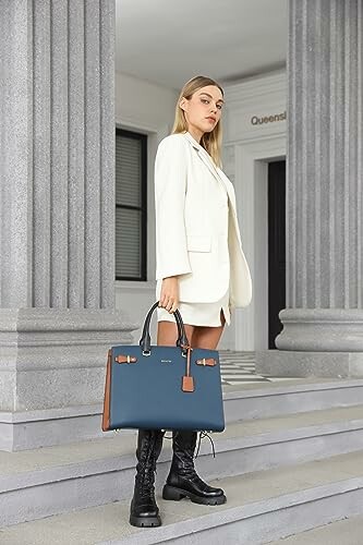 Woman in white suit with blue handbag standing on steps. 