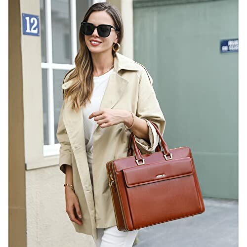 Woman in trench coat holding a brown leather handbag and wearing sunglasses.